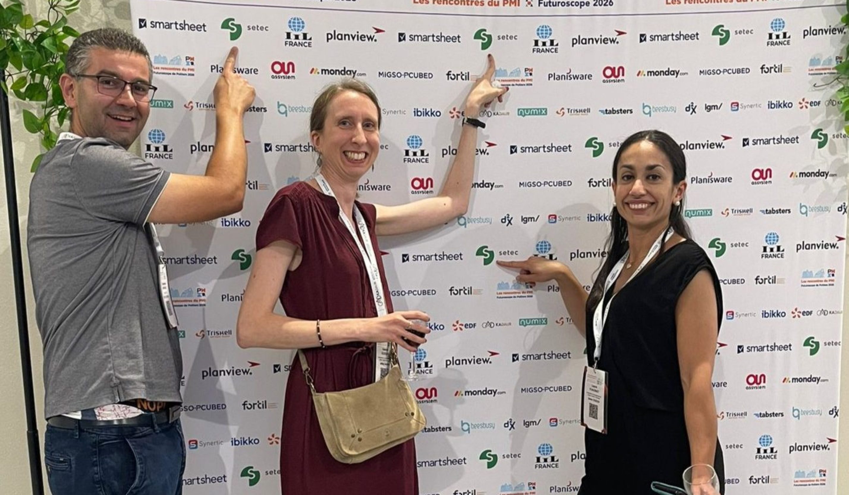 Three persons posing for a picture and pointing setec logo in the photo stand behind them.